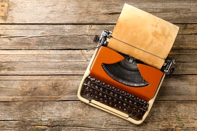 Photo of Vintage typewriter with sheet of parchment paper on wooden table, top view. Space for text
