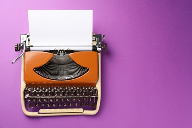 Photo of Vintage typewriter with sheet of paper on purple background, top view. Space for text
