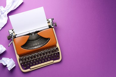 Photo of Vintage typewriter with sheet and crumpled paper on purple background, top view. Space for text
