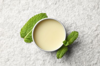 Photo of Mint lip balm and green leaves on beige textured table, top view. Cosmetic product