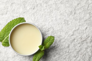 Photo of Mint lip balm and green leaves on beige textured background, top view. Space for text