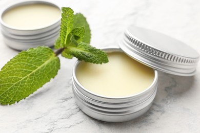 Photo of Mint lip balms and green leaves on beige textured table, closeup. Cosmetic product