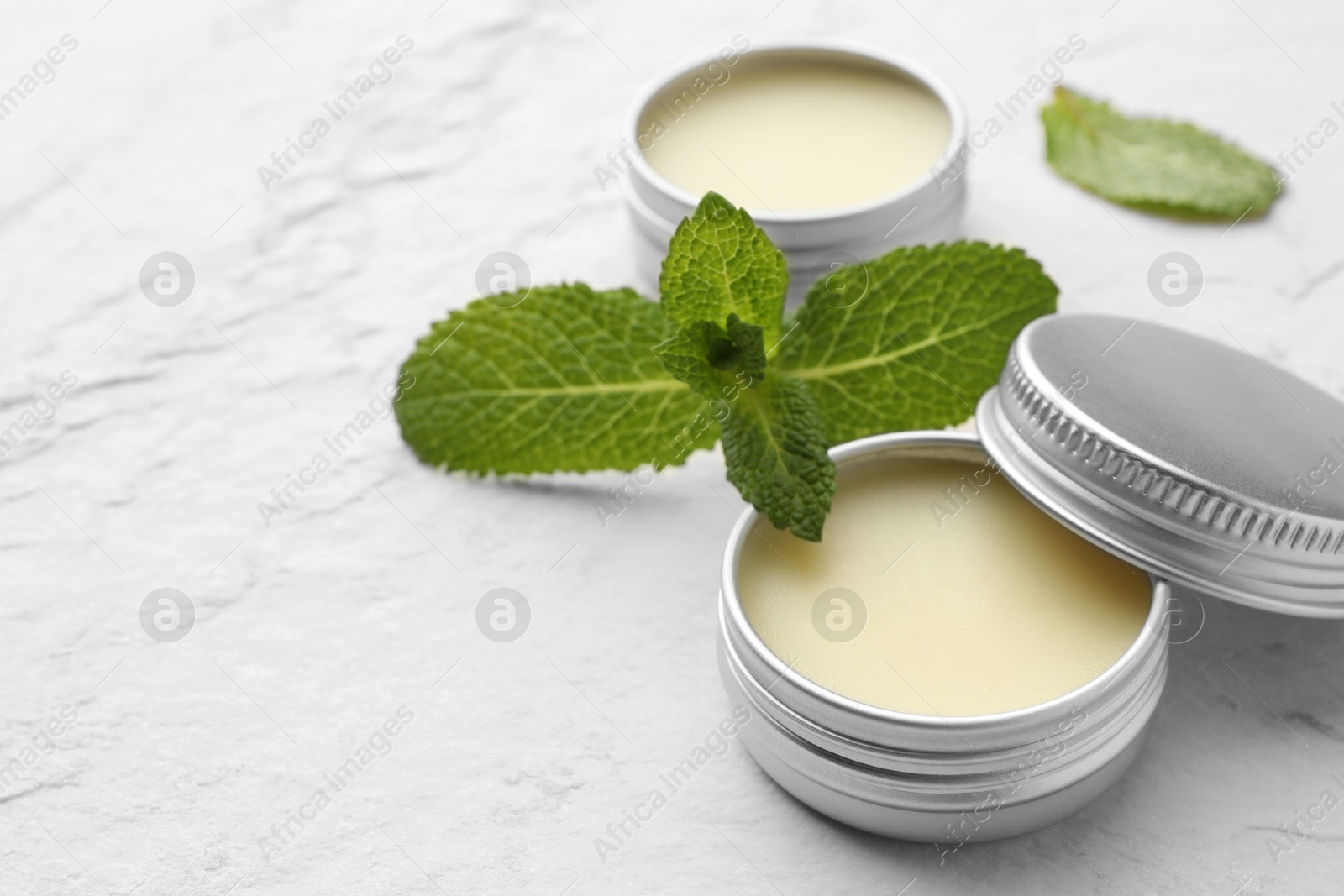 Photo of Mint lip balms and green leaves on beige textured table, closeup. Space for text