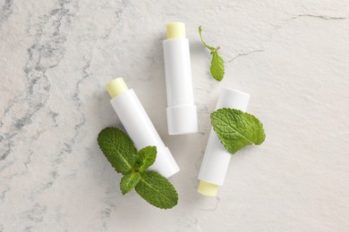 Photo of Mint lip balms and green leaves on beige textured table, flat lay. Cosmetic product