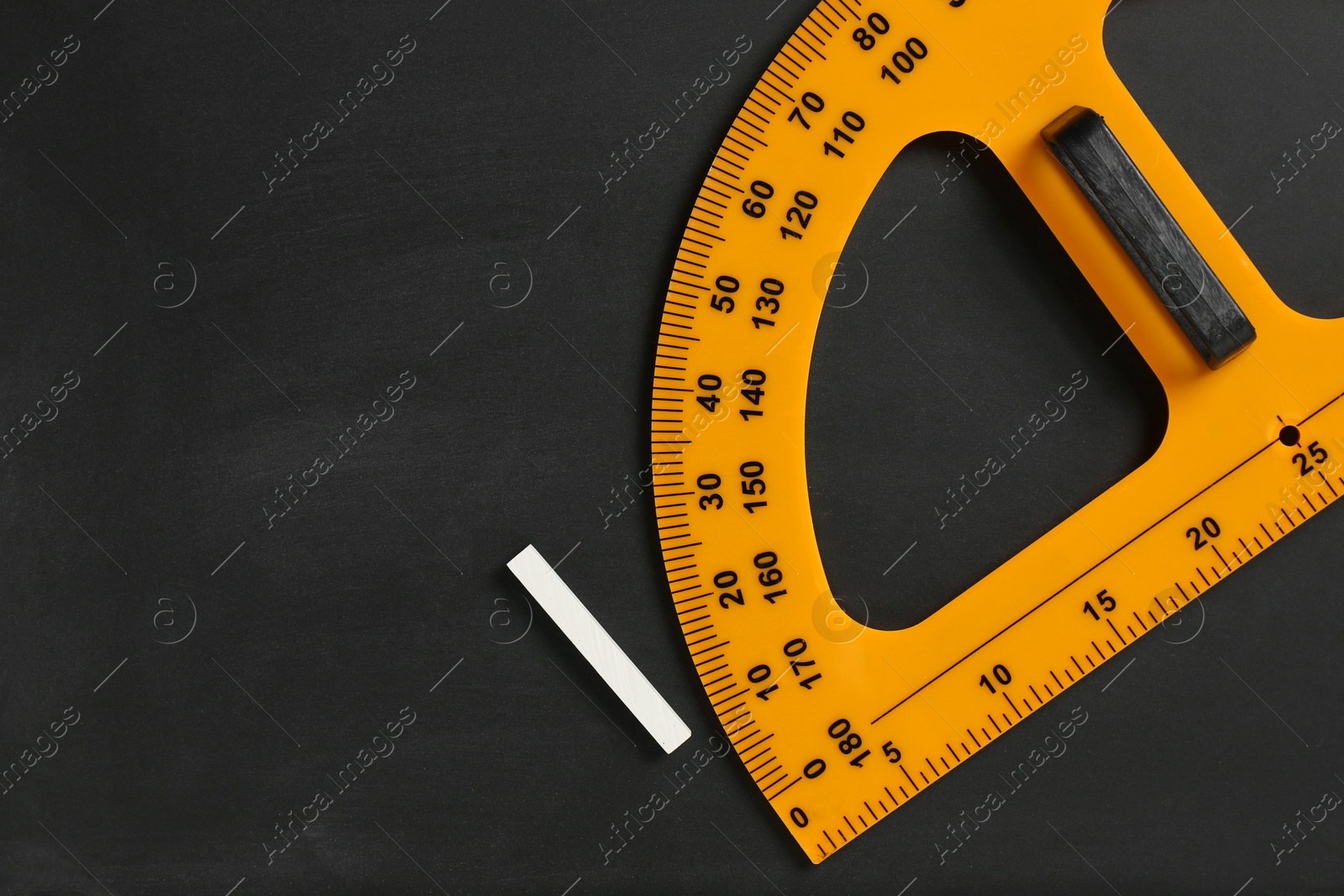 Photo of Protractor ruler and chalk on black chalkboard, top view. Space for text