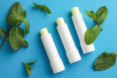 Photo of Natural lip balms and mint leaves on light blue background, flat lay