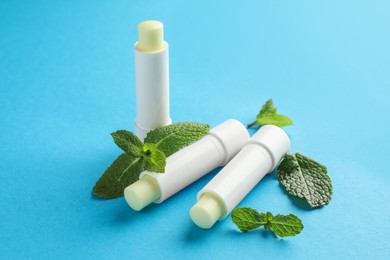 Photo of Natural lip balms and mint leaves on light blue background