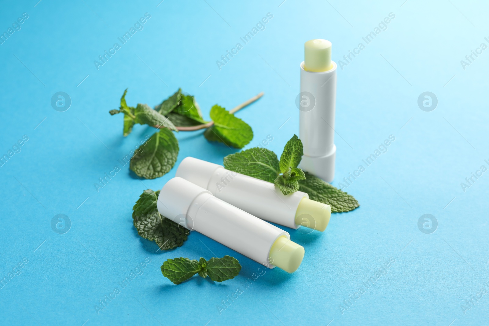 Photo of Natural lip balms and mint leaves on light blue background