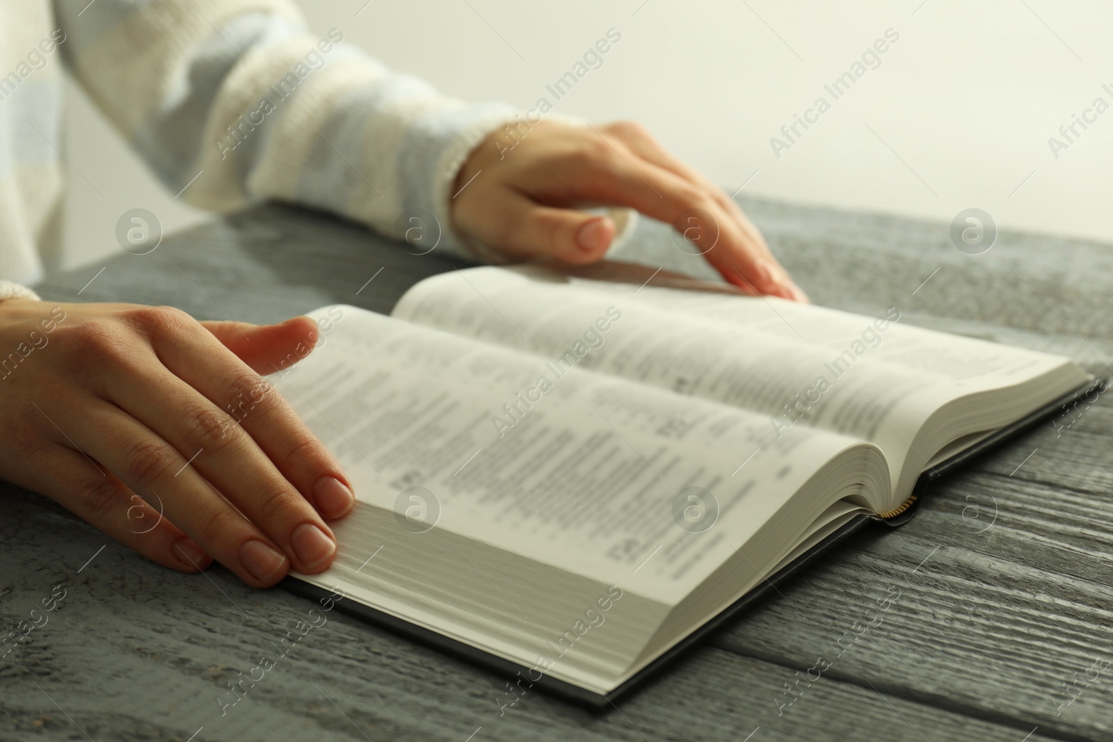 Photo of Woman with open Holy Bible at wooden table, closeup