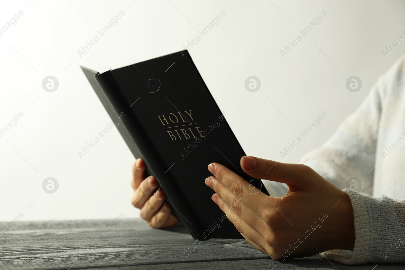 Photo of Woman with open Holy Bible at wooden table, closeup