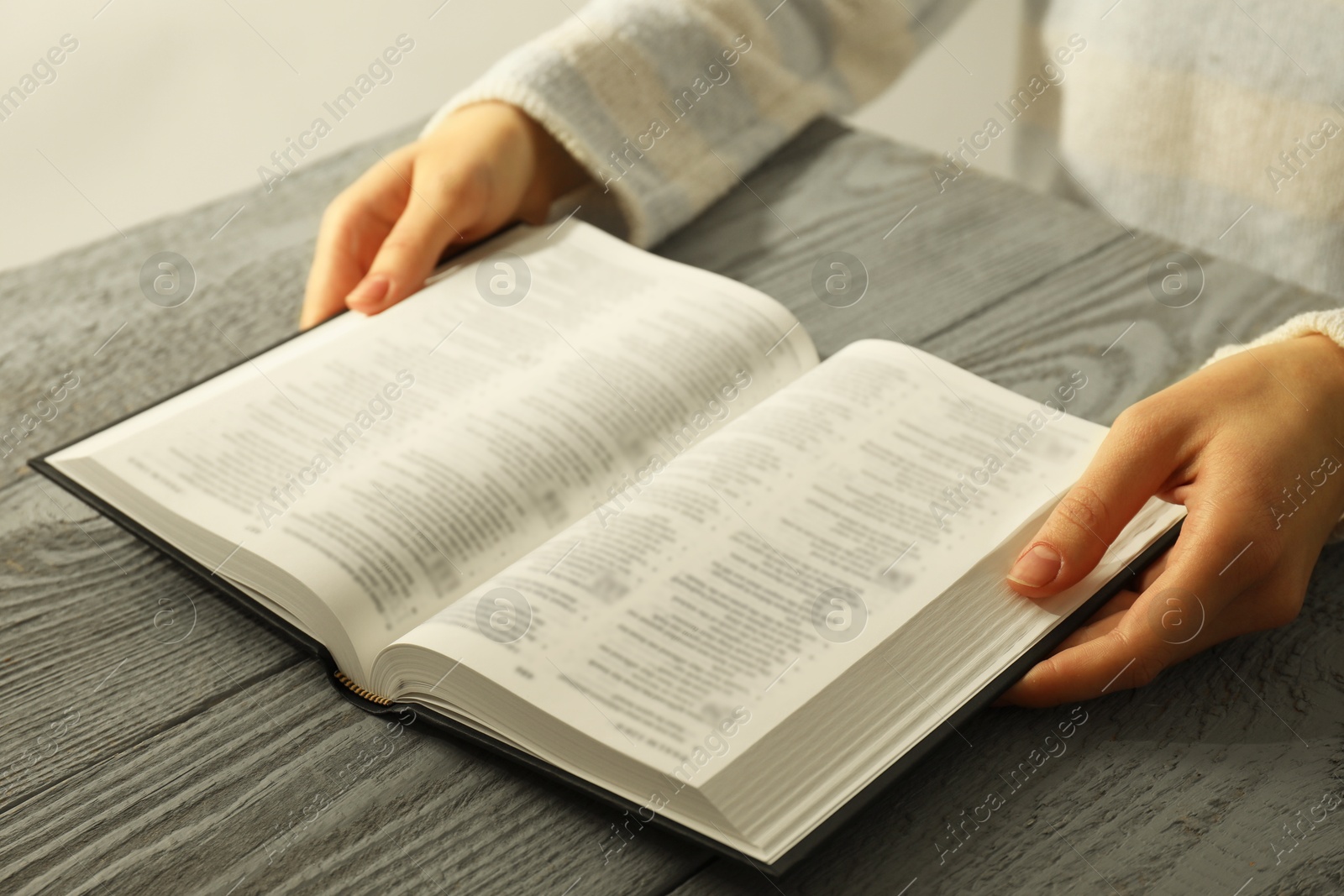 Photo of Woman with open Holy Bible in English language at wooden table, closeup