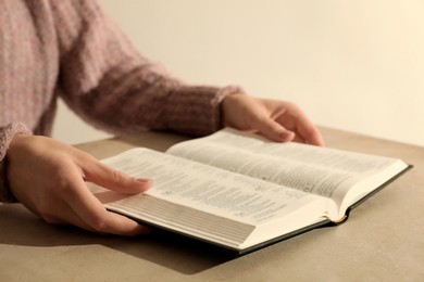 Photo of Woman reading Holy Bible at beige table, closeup