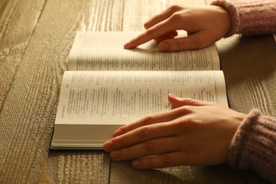 Photo of Woman reading Holy Bible in English language at wooden table, closeup