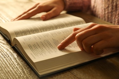 Photo of Woman reading Holy Bible in English language at wooden table, closeup