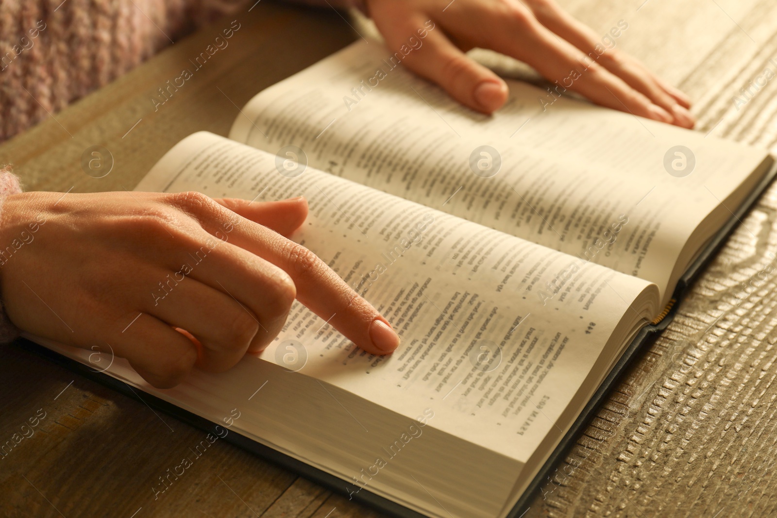 Photo of Woman reading Holy Bible at wooden table, closeup