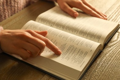 Photo of Woman reading Holy Bible at wooden table, closeup