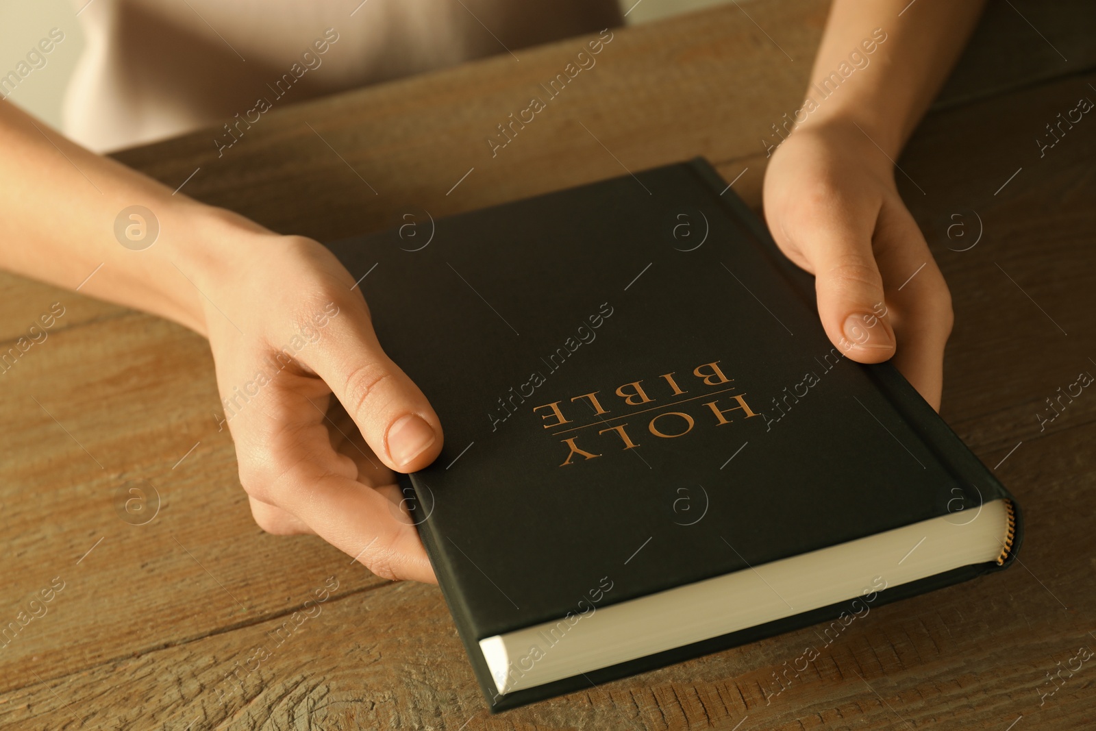 Photo of Woman with hardcover Holy Bible at wooden table, closeup