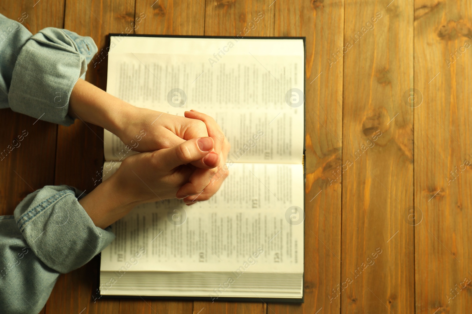 Photo of Woman with open Holy Bible praying at wooden table, top view