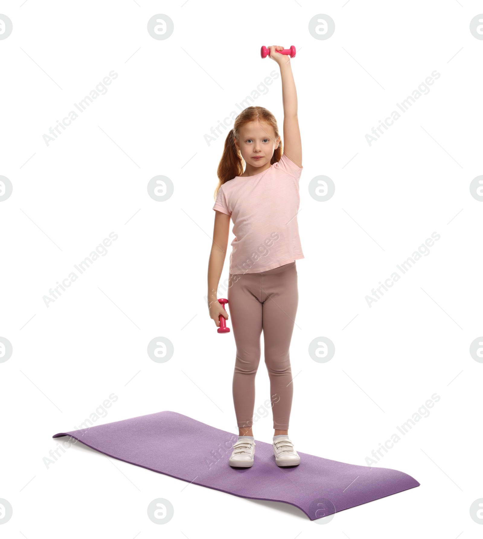 Photo of Cute little girl exercising with dumbbells on mat against white background