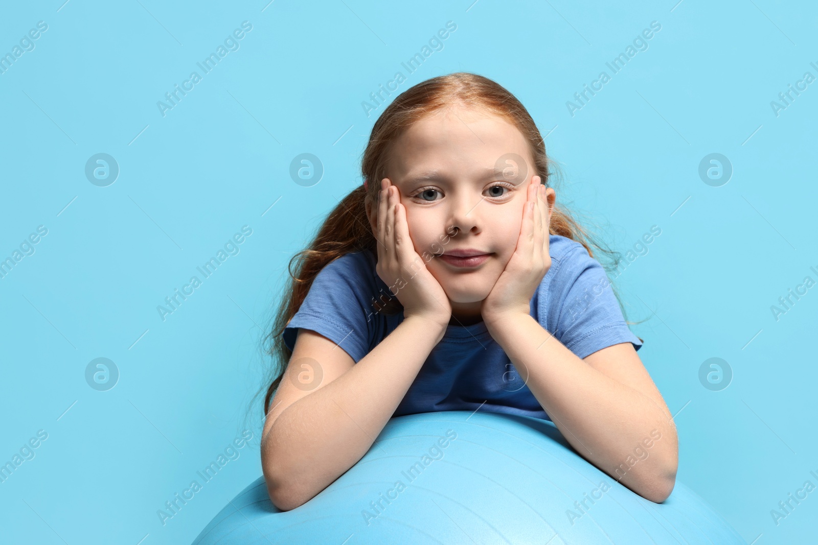 Photo of Cute little girl with fitness ball on light blue background, space for text