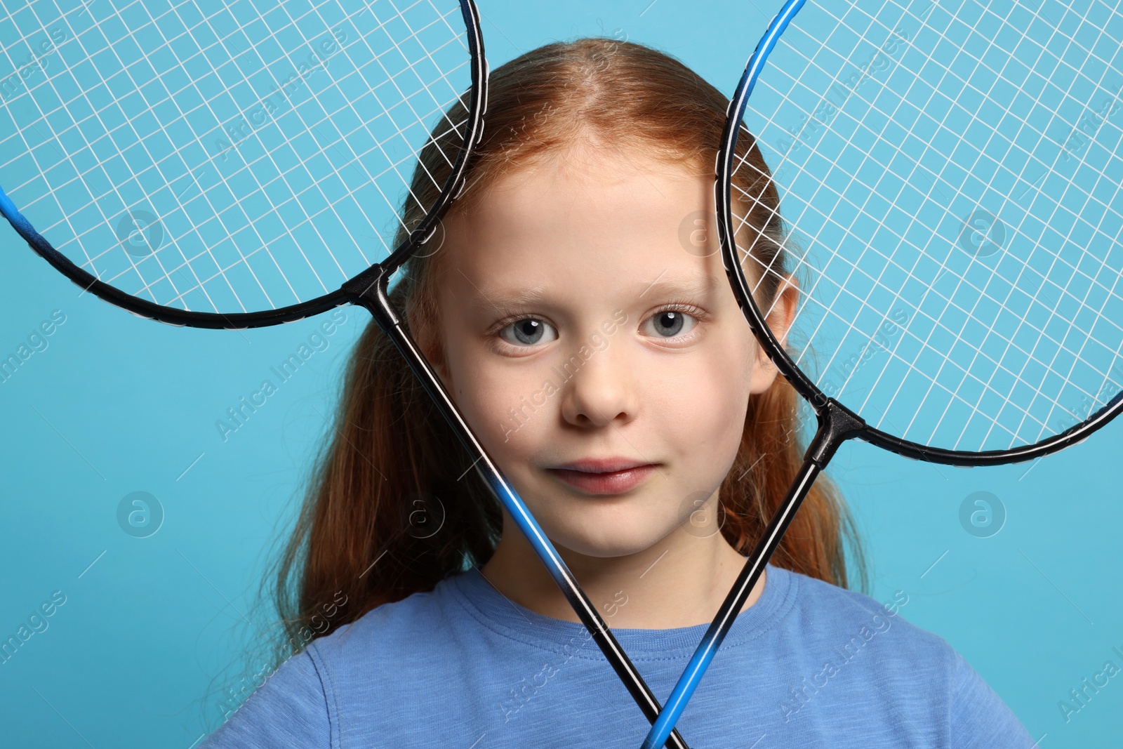 Photo of Little girl with badminton rackets on light blue background