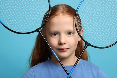 Photo of Little girl with badminton rackets on light blue background