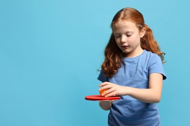 Photo of Little girl with ping pong racket and ball on light blue background, space for text