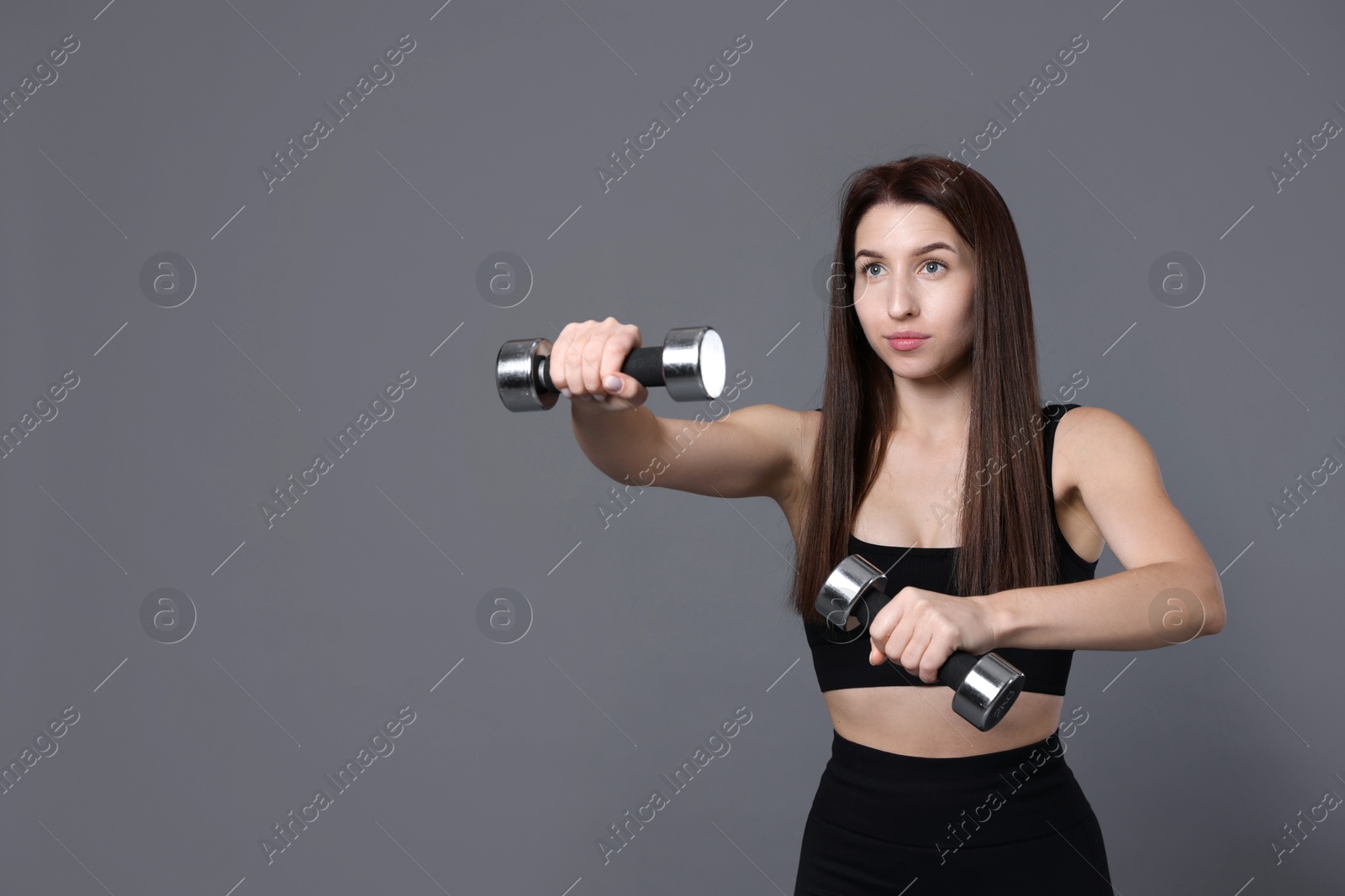 Photo of Woman in sportswear exercising with dumbbells on grey background, space for text