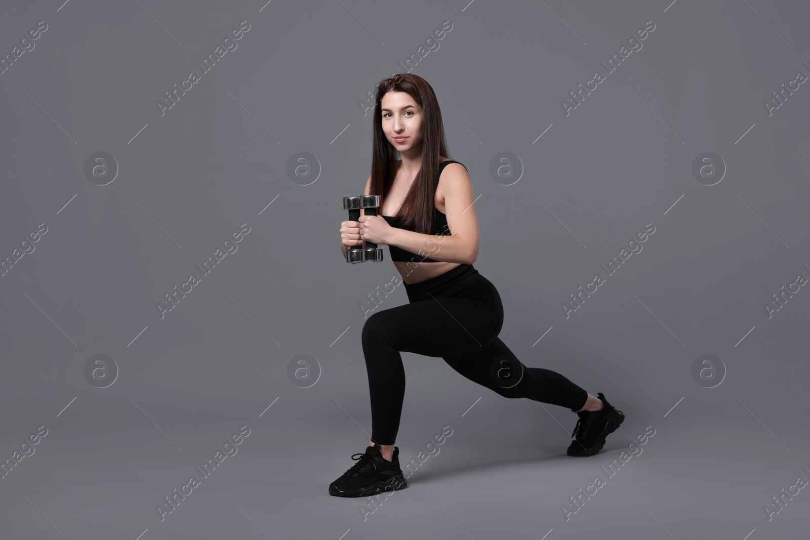 Photo of Woman in sportswear exercising with dumbbells on grey background, space for text