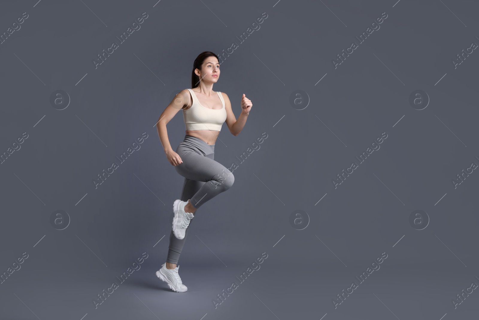 Photo of Woman in sportswear exercising on grey background