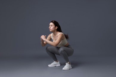 Photo of Woman in sportswear exercising on grey background