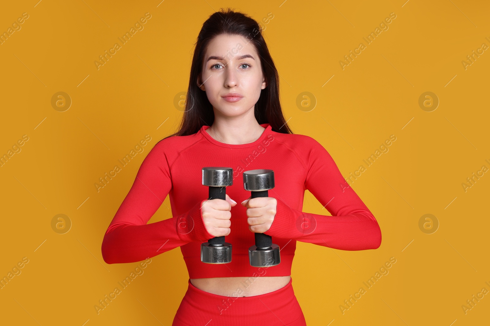 Photo of Woman in sportswear exercising with dumbbells on orange background