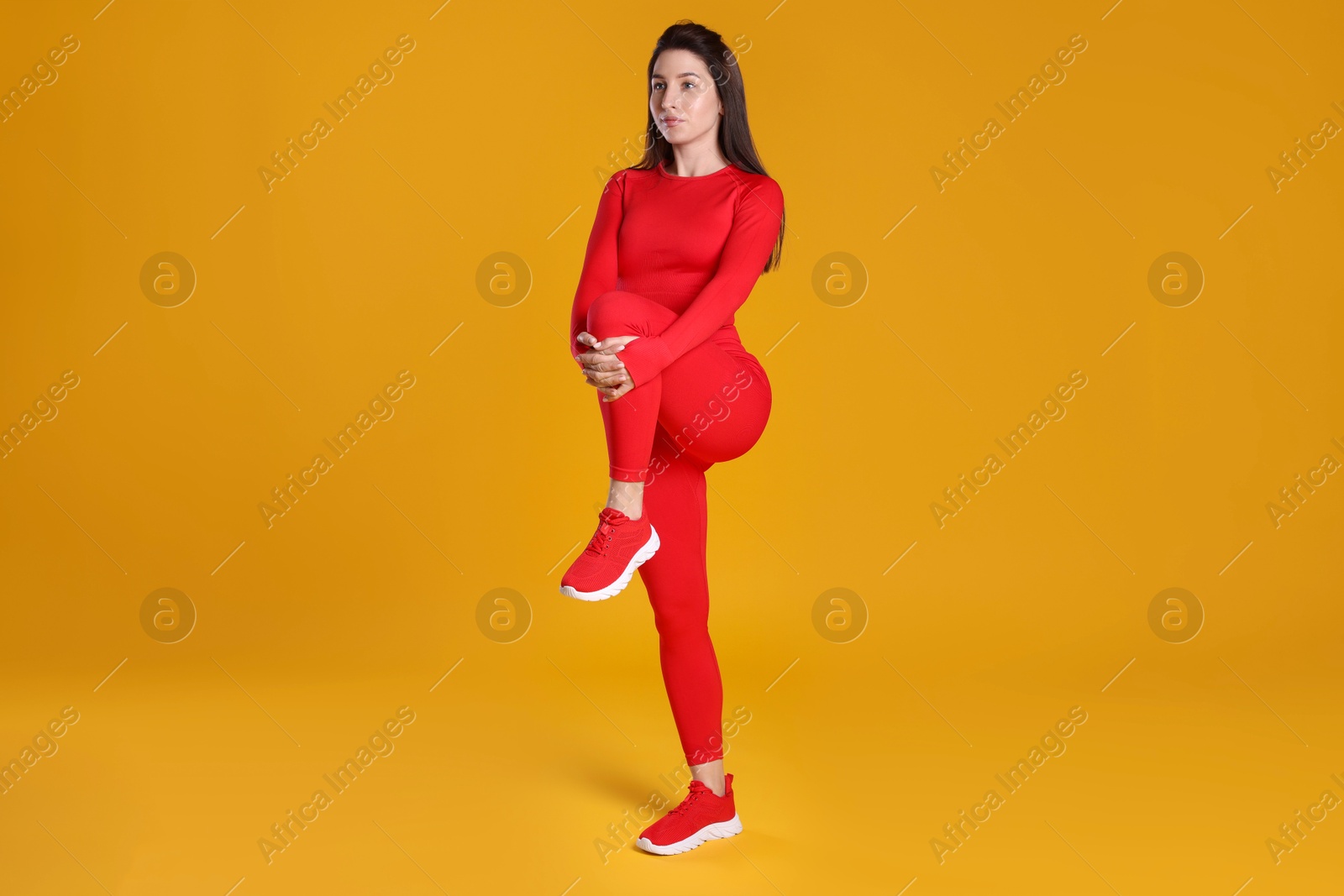 Photo of Woman in sportswear exercising on orange background