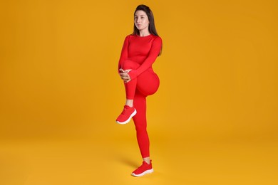 Woman in sportswear exercising on orange background