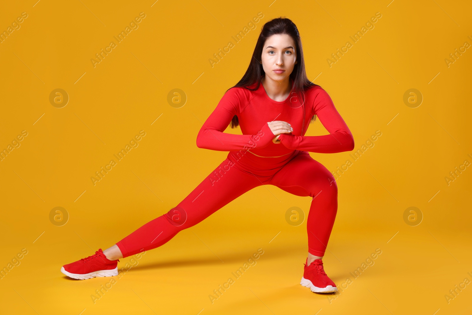 Photo of Woman in sportswear exercising on orange background