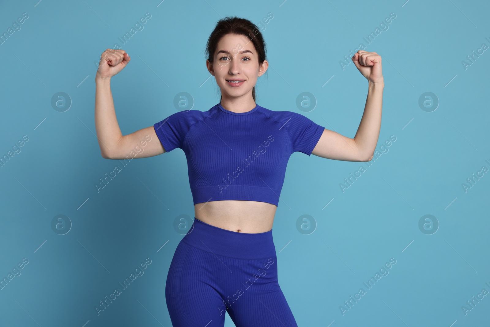 Photo of Woman in sportswear showing her biceps on light blue background