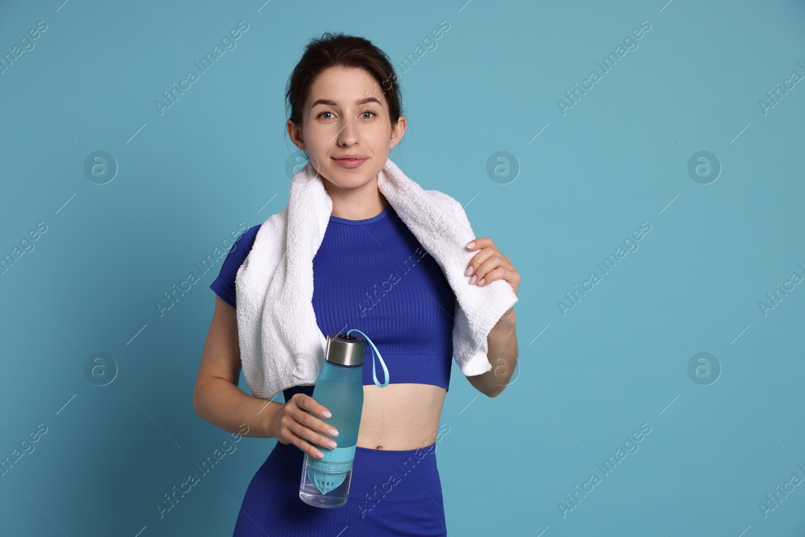 Photo of Woman in sportswear with bottle of water and towel on light blue background