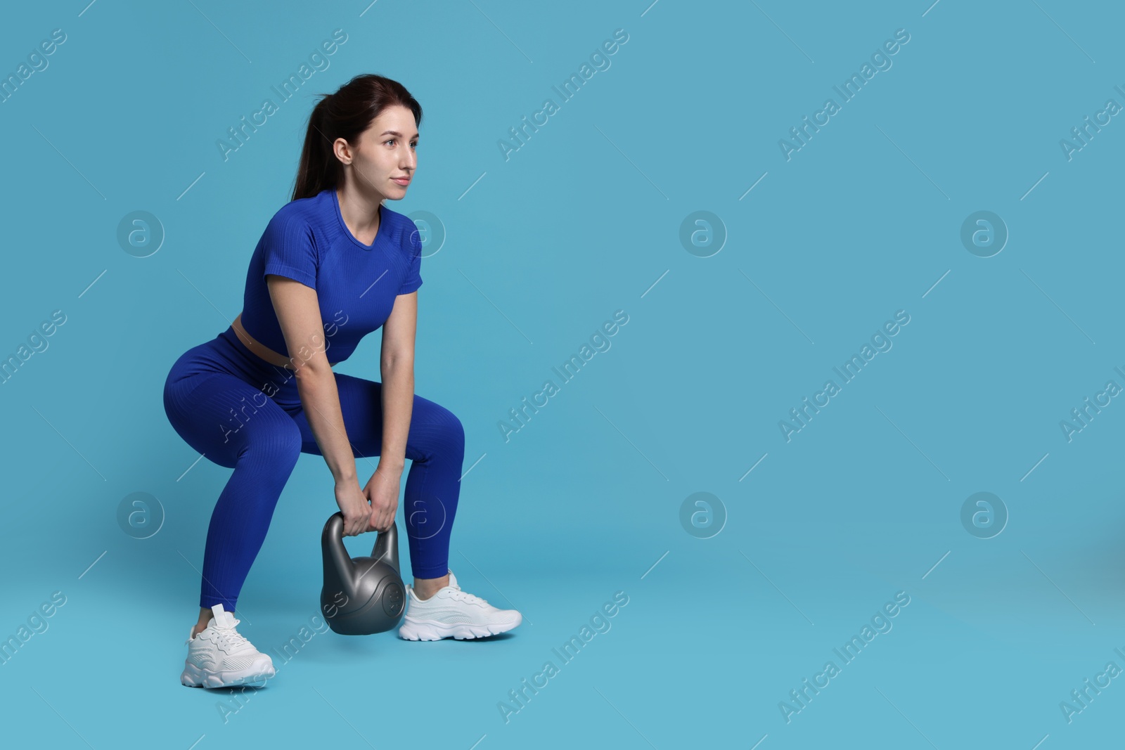 Photo of Woman in sportswear exercising with kettlebell on light blue background, space for text