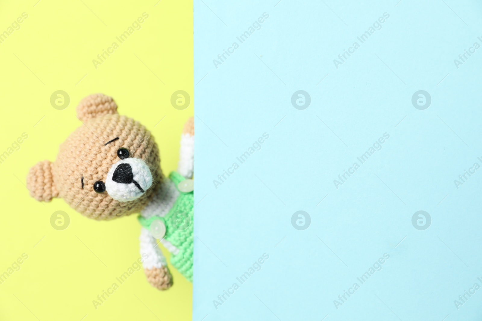 Photo of Cute toy bear peeking out of blank card on yellow background. Space for text