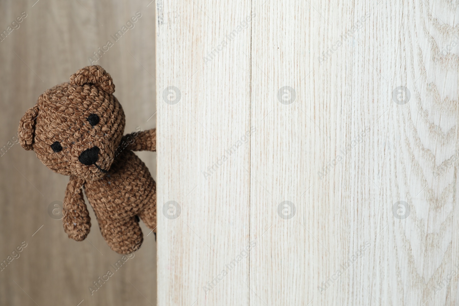 Photo of Cute toy bear peeking out of wooden board. Space for text