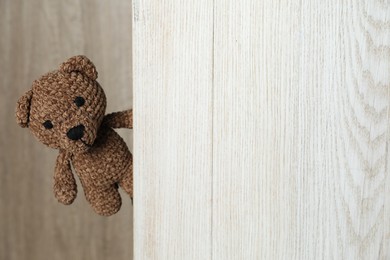 Photo of Cute toy bear peeking out of wooden board. Space for text