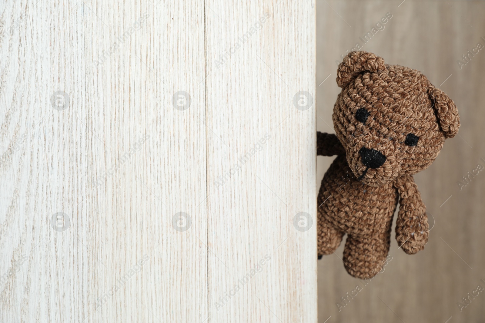 Photo of Cute toy bear peeking out of wooden board. Space for text