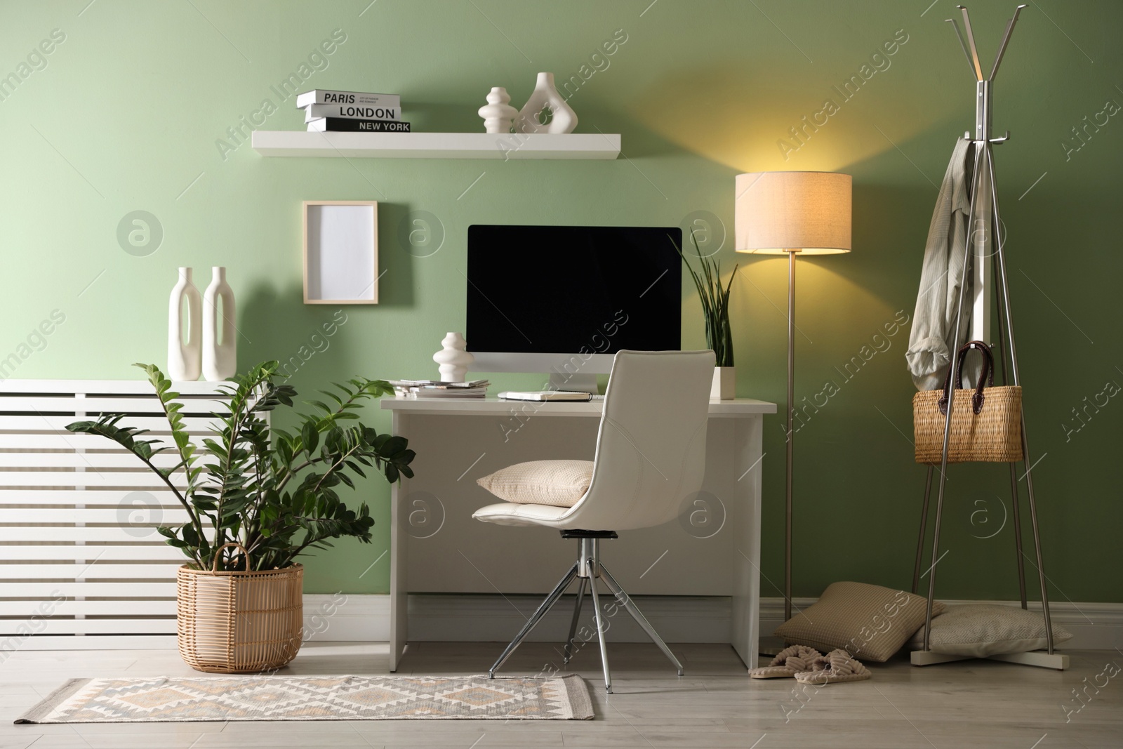 Photo of Home office. Comfortable workplace with desk, computer and lamp near light green wall in room