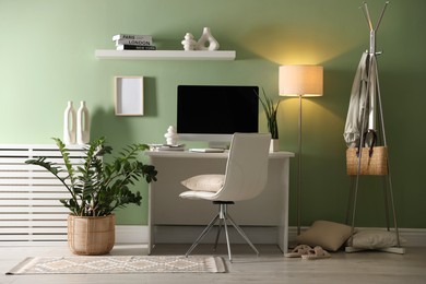 Photo of Home office. Comfortable workplace with desk, computer and lamp near light green wall in room