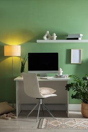 Home office. Comfortable workplace with desk, computer and lamp near light green wall in room