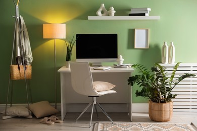 Home office. Comfortable workplace with desk, computer and lamp near light green wall in room