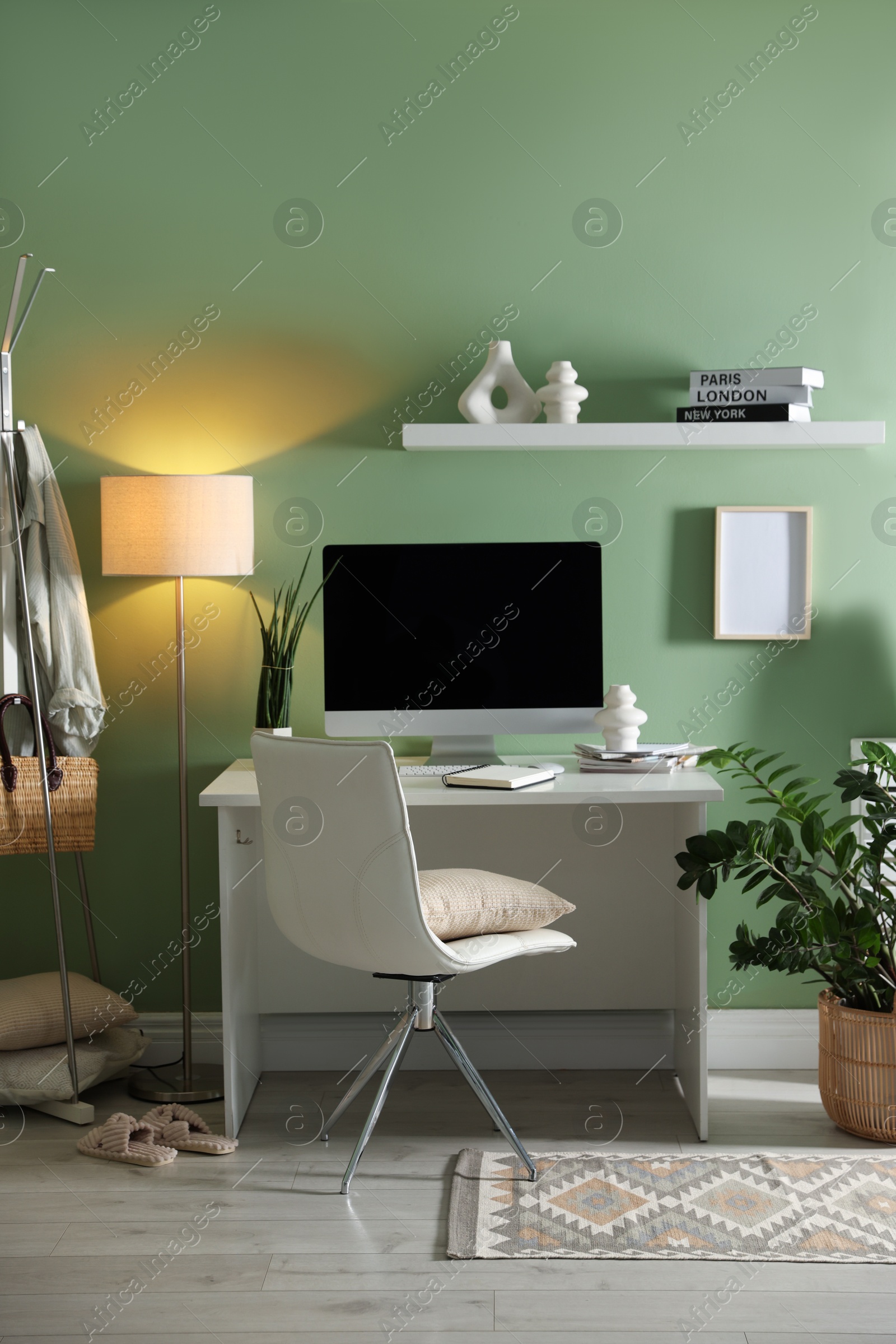 Photo of Home office. Comfortable workplace with desk, computer and lamp near light green wall in room