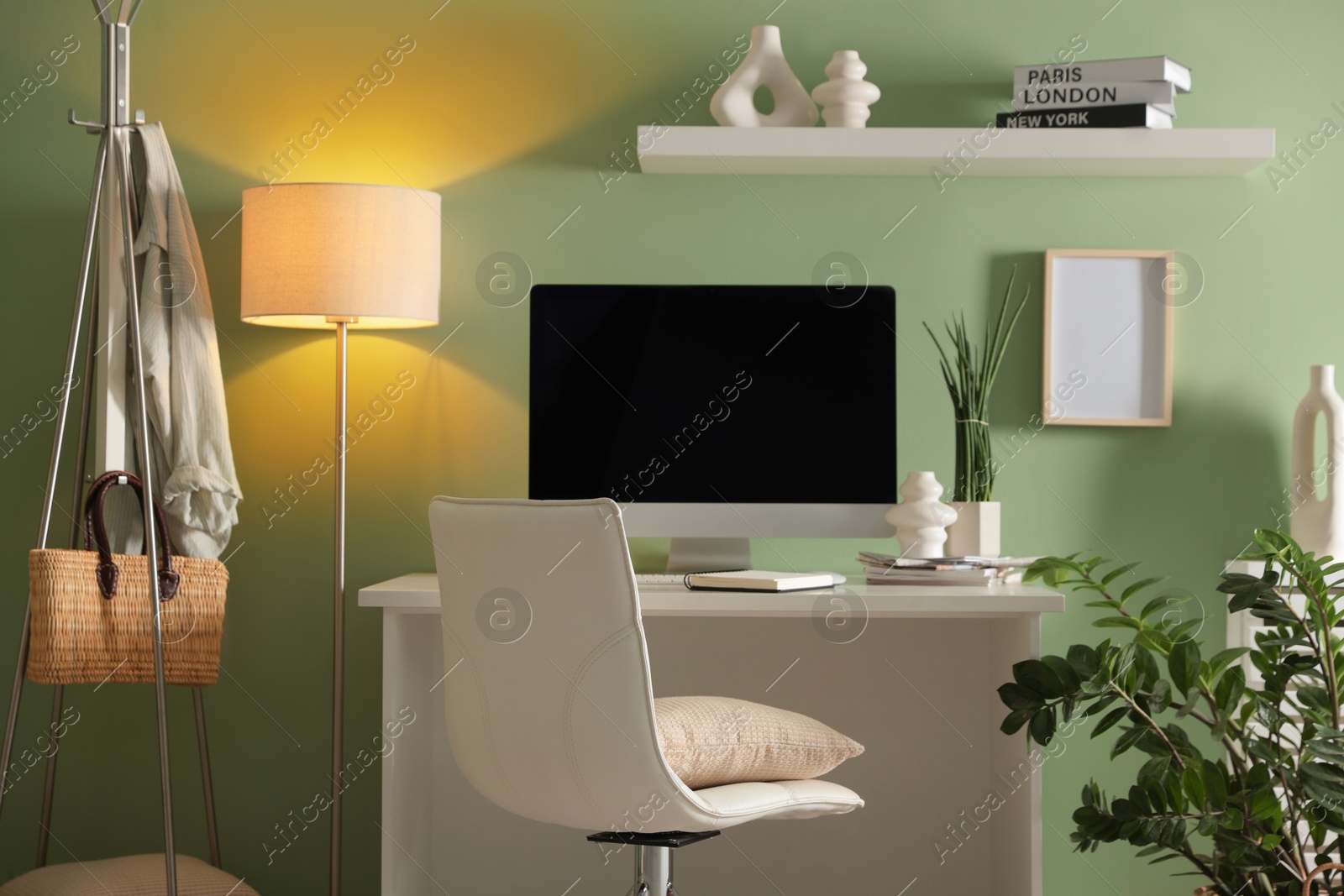 Photo of Home office. Comfortable workplace with desk, computer and lamp near light green wall in room