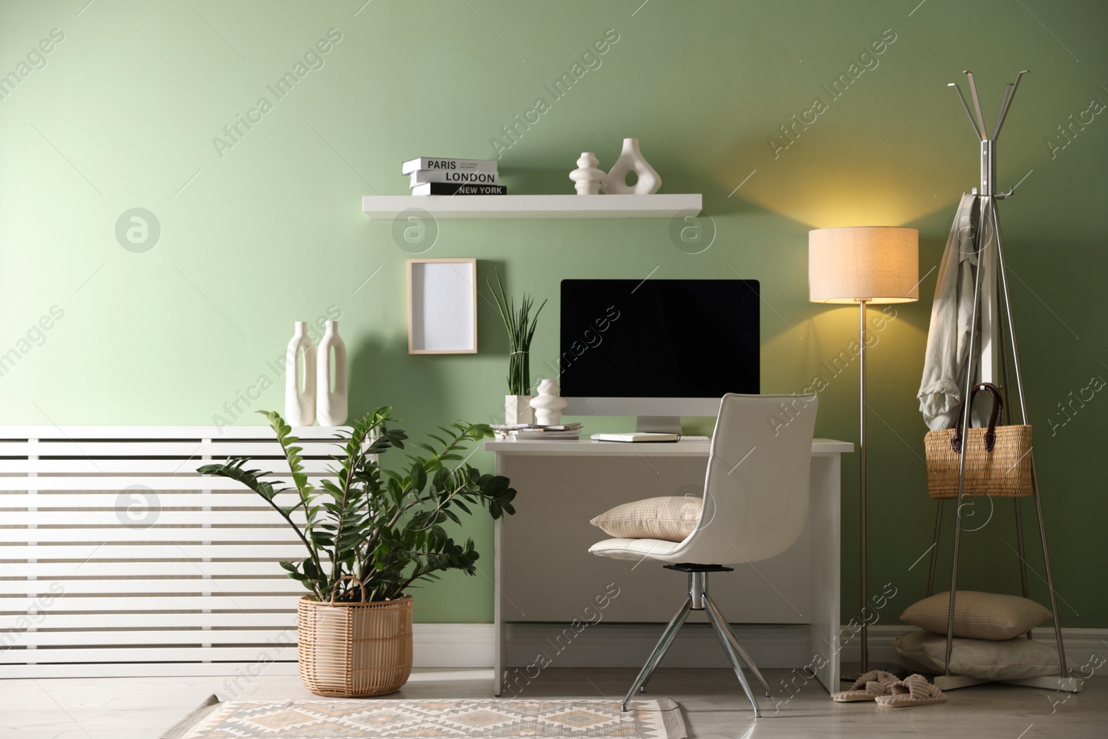 Photo of Home office. Comfortable workplace with desk, computer and lamp near light green wall in room