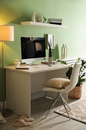 Home office. Comfortable workplace with desk, computer and lamp near light green wall in room